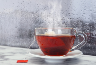 Image of Cup of hot tea near window on rainy day