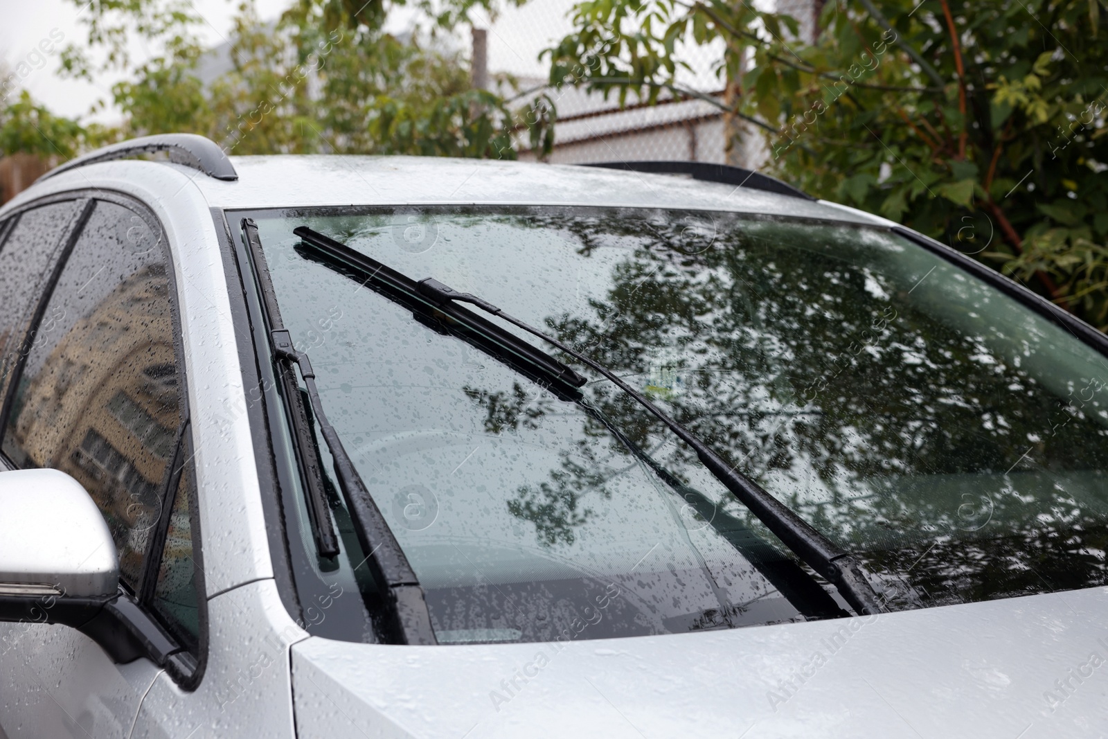 Photo of Wipers cleaning raindrops from car windshield outdoors