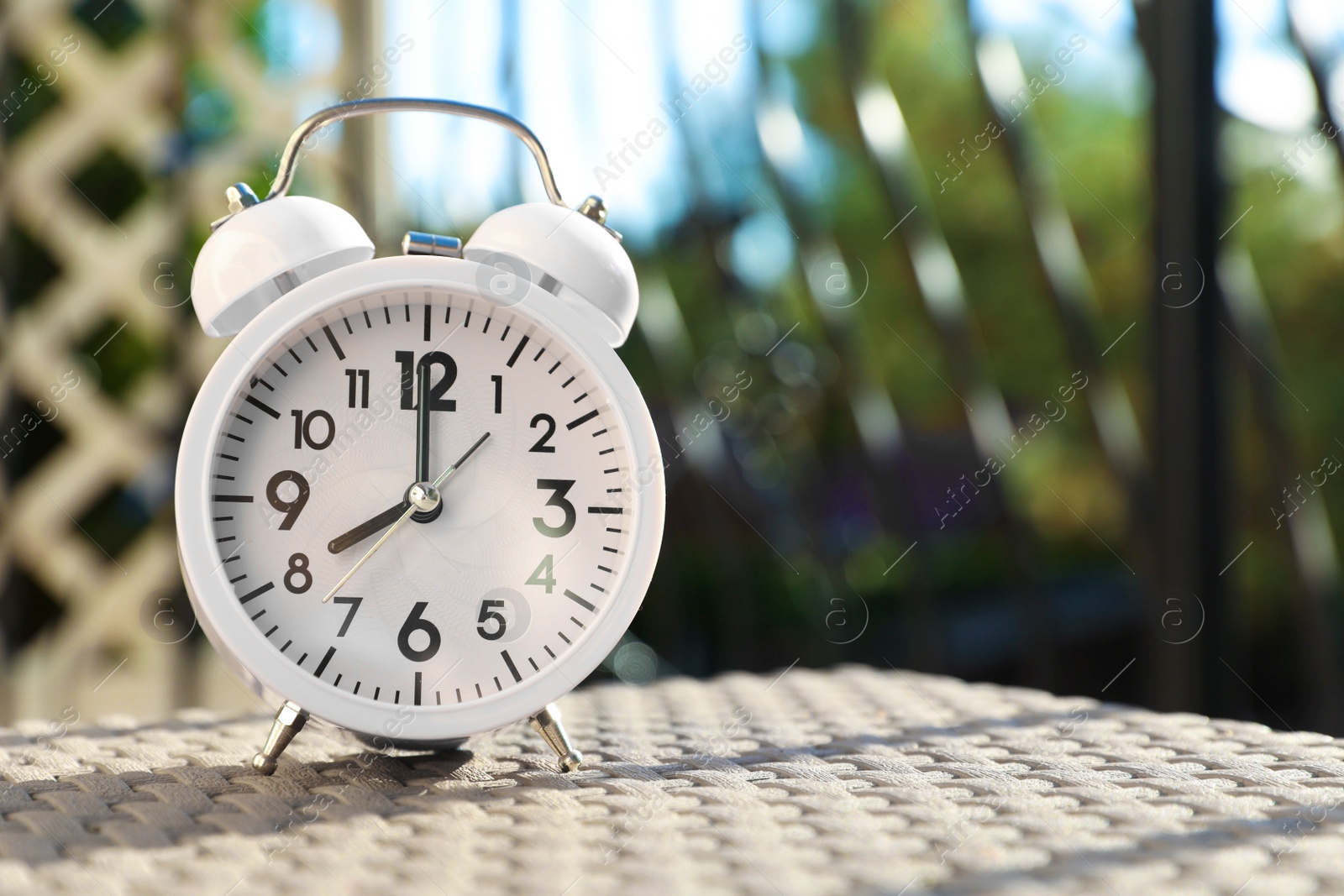 Photo of Pink alarm clock on table outdoors at sunny morning. Space for text