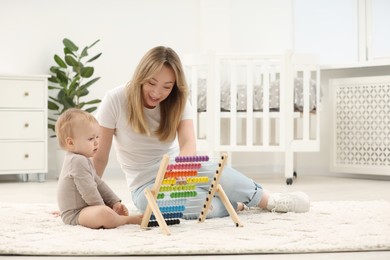 Children toys. Happy mother and her little son playing with wooden abacus on rug at home