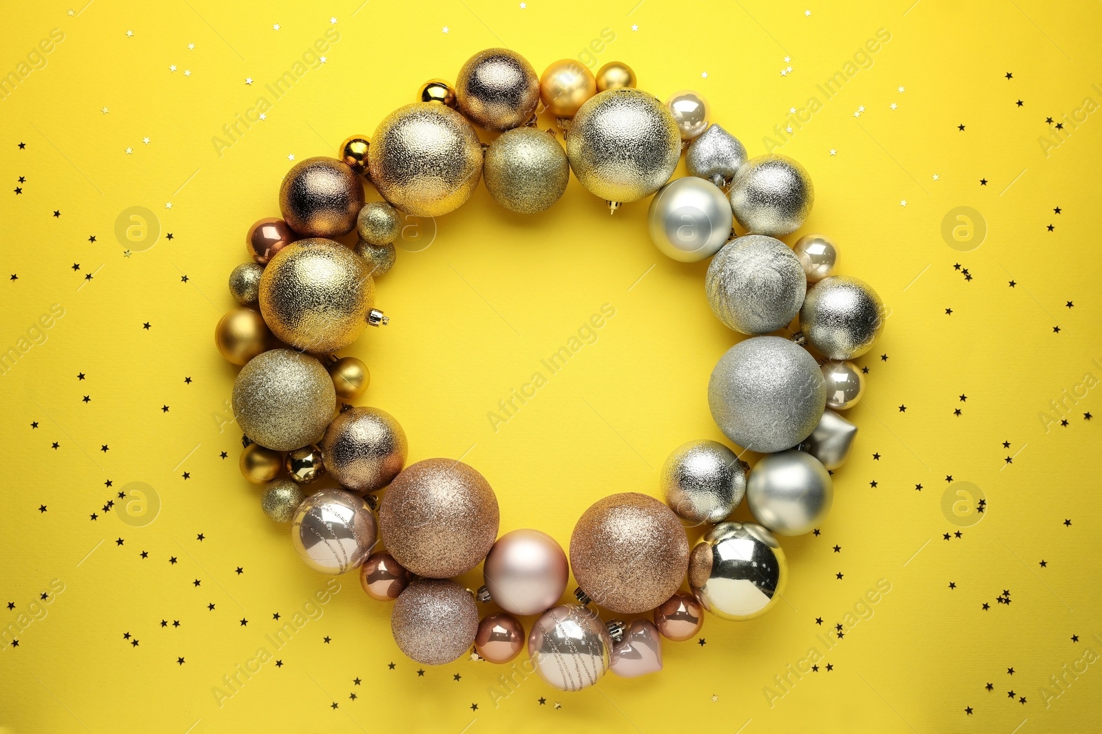 Photo of Bright festive wreath made of Christmas balls on yellow background, top view. Space for text