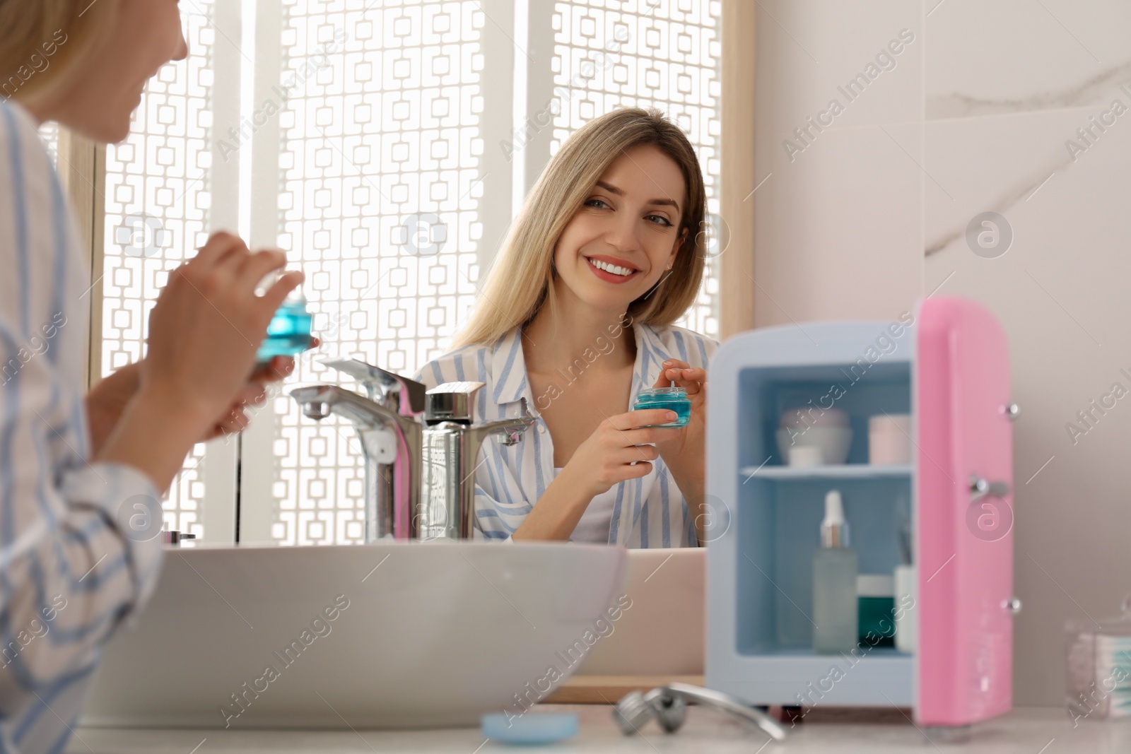 Photo of Woman using cosmetic product near mini fridge indoors