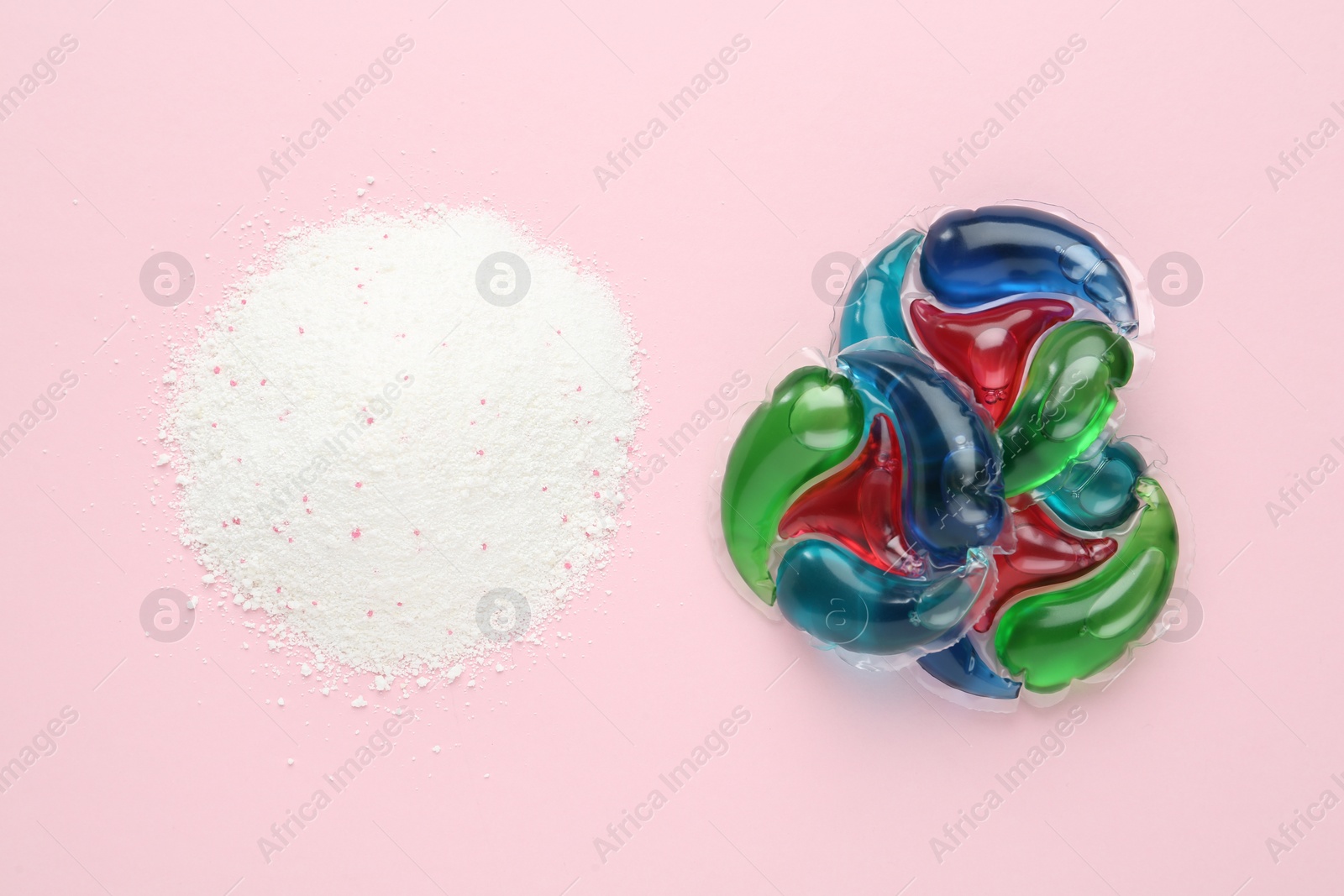 Photo of Laundry capsules and washing powder on pink background, flat lay