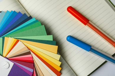 Photo of Color palette and pens on notebook, top view