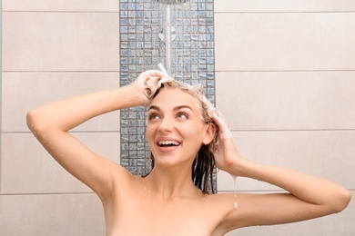 Photo of Beautiful young woman washing hair in shower at home
