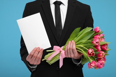 Photo of Man with beautiful bouquet and greeting card on light blue background, closeup