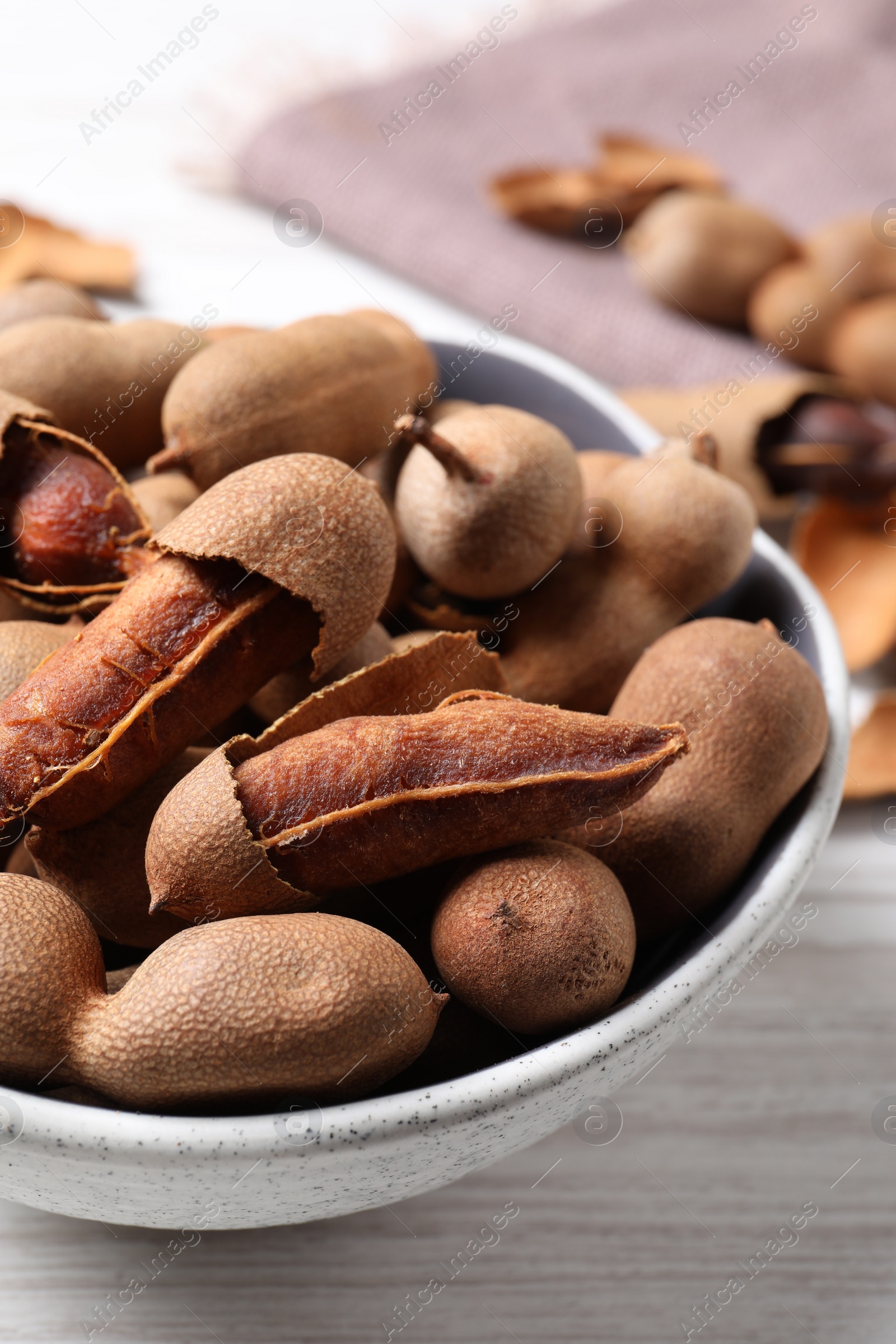 Photo of Delicious ripe tamarinds in ceramic bowl on white wooden table, closeup