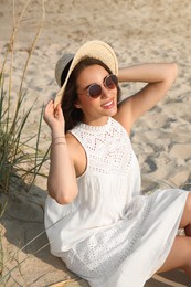 Beautiful young woman with straw hat and sunglasses on beach. Stylish headdress