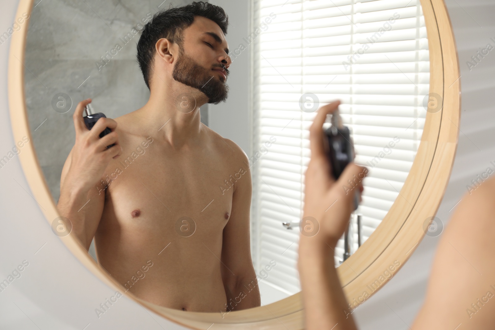 Photo of Man spraying luxury perfume near mirror indoors