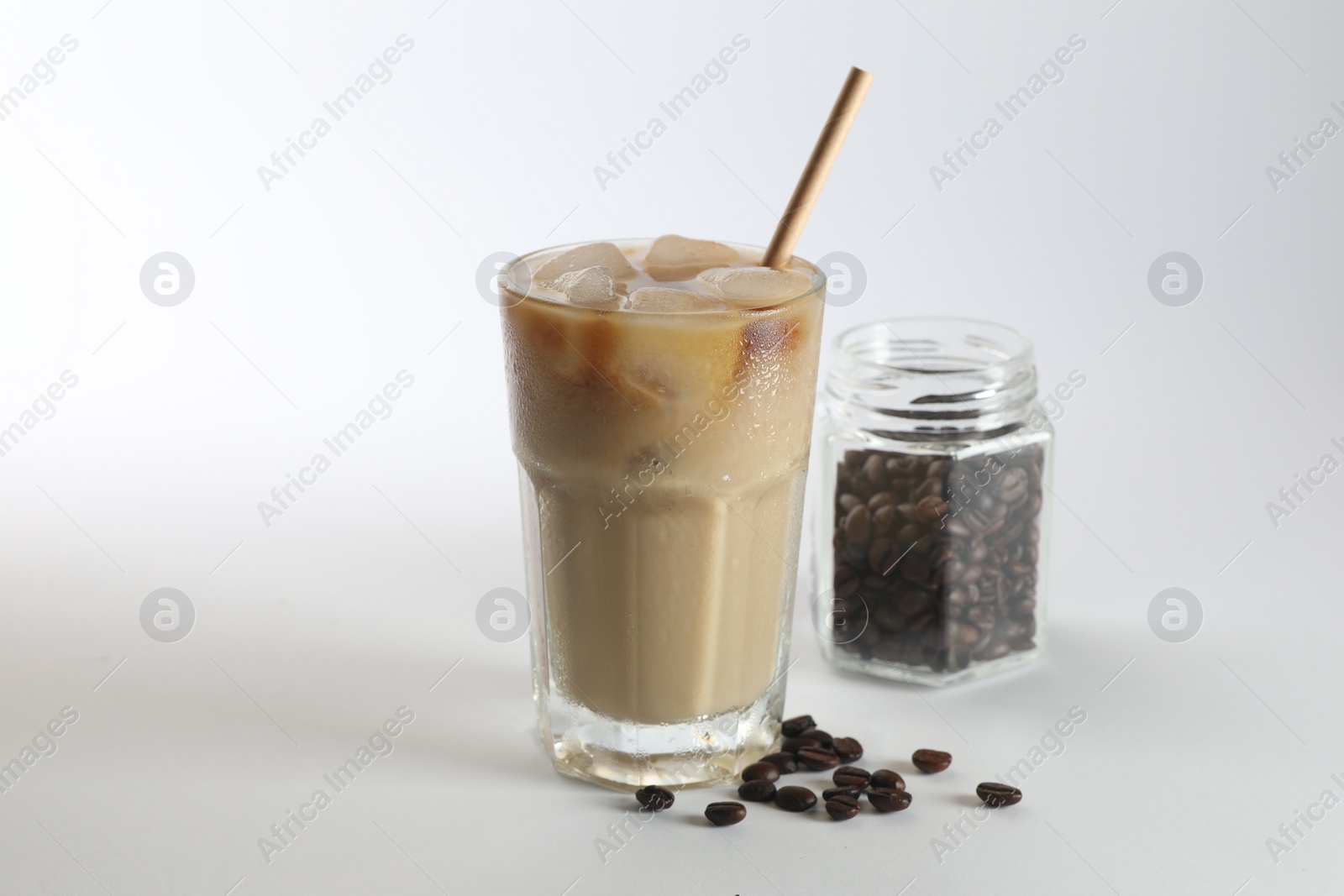 Photo of Iced coffee with milk in glass and jar of roasted beans on white background