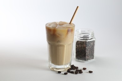 Photo of Iced coffee with milk in glass and jar of roasted beans on white background