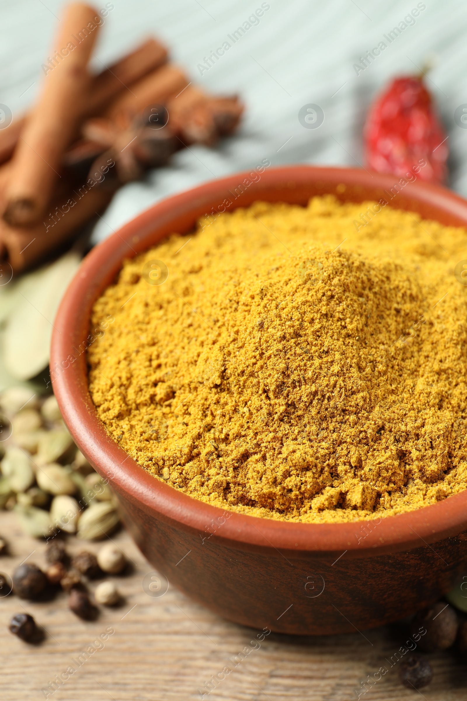 Photo of Curry powder in bowl and other spices on wooden table, closeup