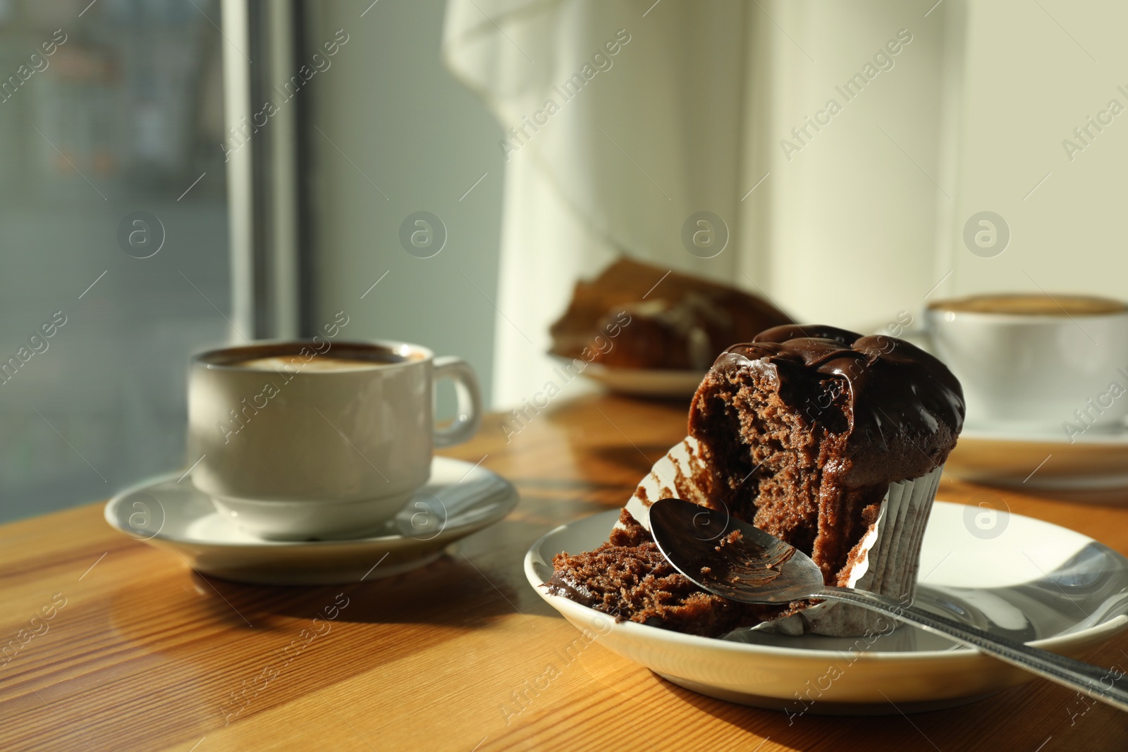 Photo of Cup of fresh aromatic coffee and cupcake at table in cafe