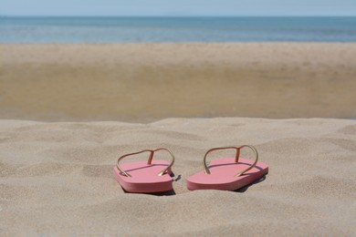 Photo of Stylish pink flip flops on sandy beach near sea, space for text