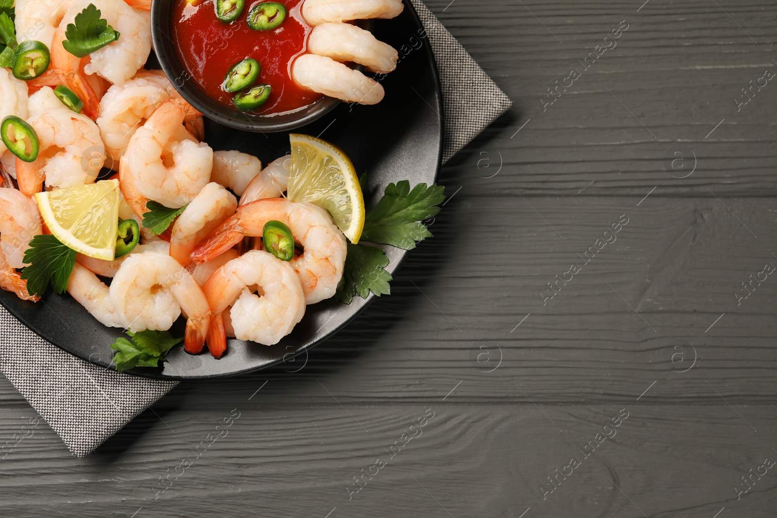 Photo of Tasty boiled shrimps with cocktail sauce, chili, parsley and lemon on grey wooden table, top view. Space for text