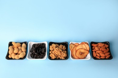 Photo of Bowls with dried fruits and nuts on light blue background, above view. Space for text
