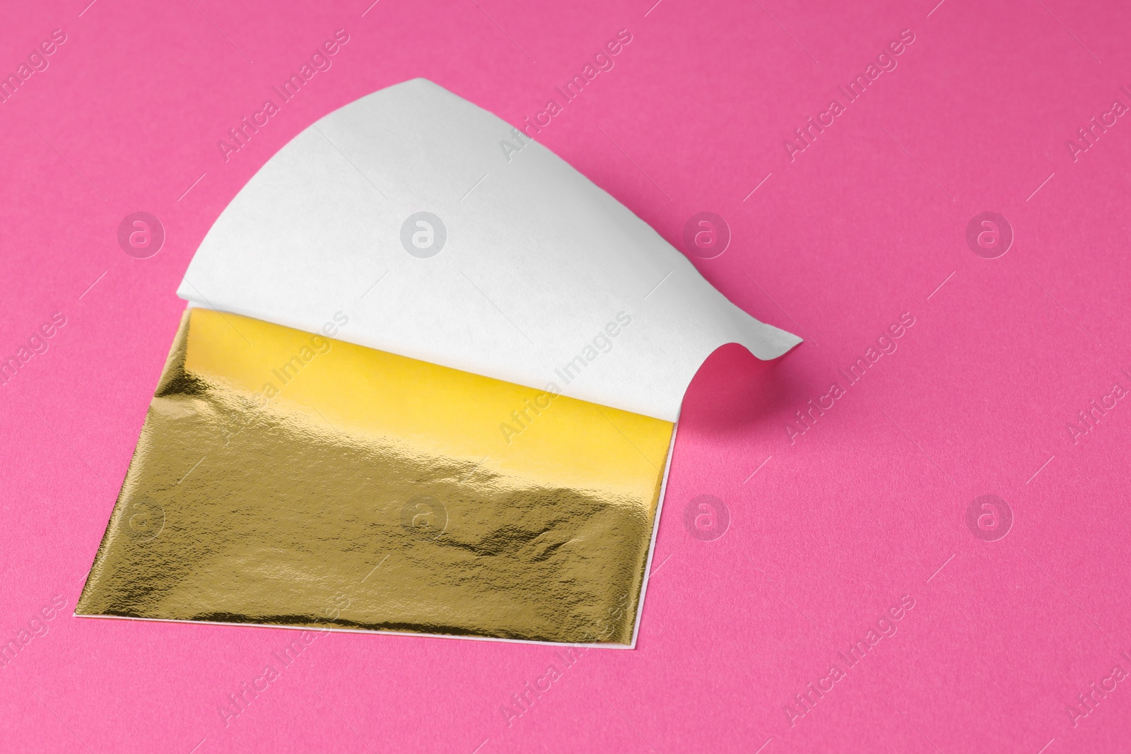 Photo of Edible gold leaf sheet on pink background, closeup