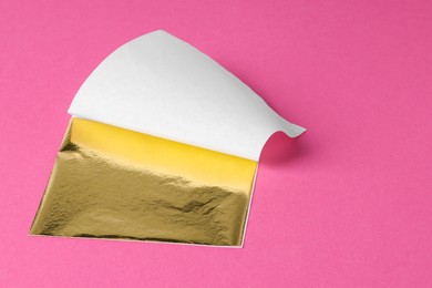 Photo of Edible gold leaf sheet on pink background, closeup