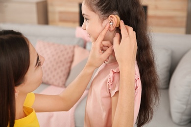 Young woman putting hearing aid in daughter's ear indoors