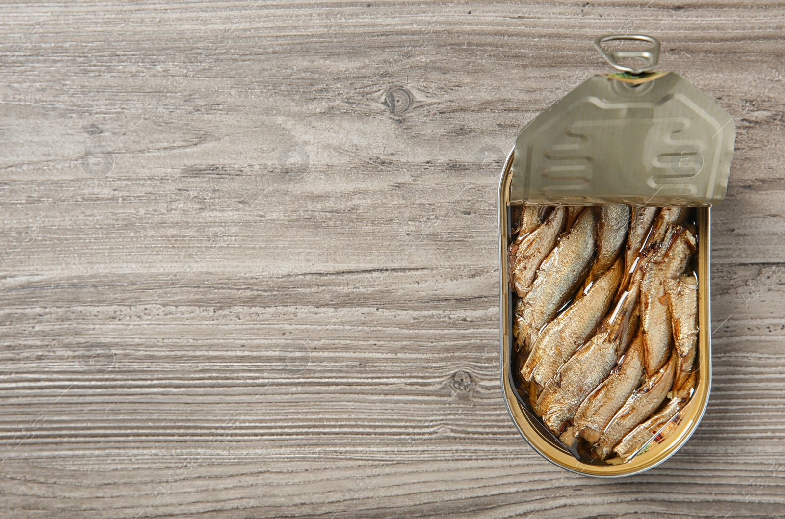Photo of Open tin can of sprats on wooden background, top view. Space for text