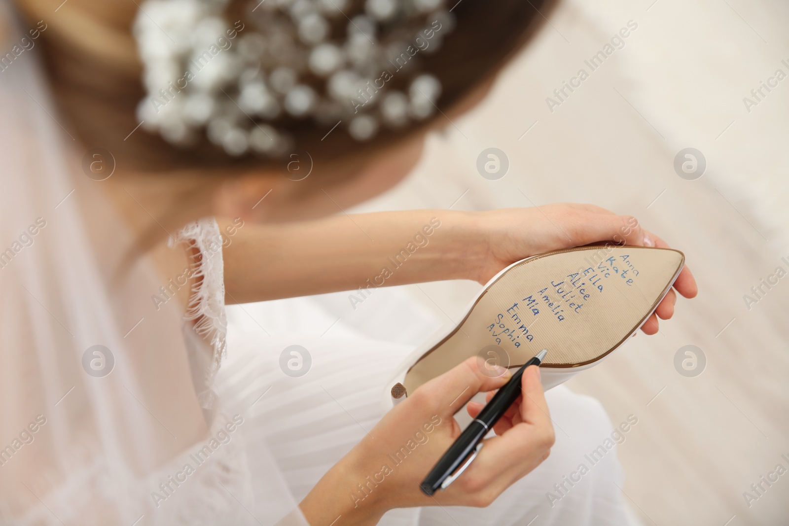 Photo of Young bride writing her single friends names on shoe indoors, closeup. Wedding superstition