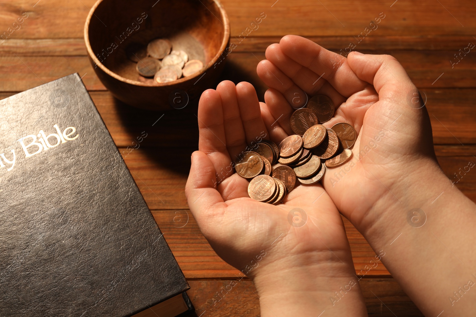 Photo of Donate and give concept. Woman holding coins, closeup. Bible and bowl of money on wooden table