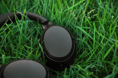 Black wireless headphones on green grass outdoors, closeup