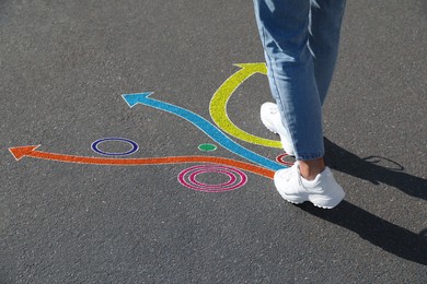 Image of Choice of way. Woman walking towards drawn marks on road, closeup. Colorful arrows pointing in different directions
