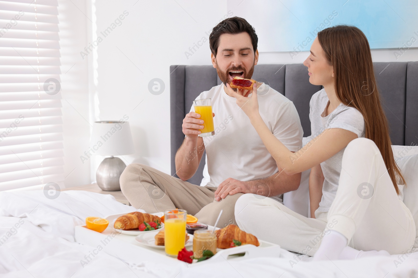 Photo of Tasty breakfast. Wife feeding her husband on bed at home. Space for text