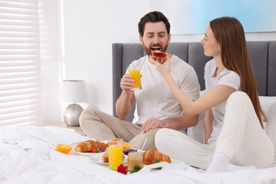 Photo of Tasty breakfast. Wife feeding her husband on bed at home. Space for text