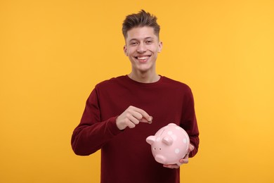 Photo of Happy man putting coin into piggy bank on yellow background