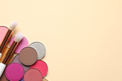 Photo of Different beautiful eye shadows and makeup brushes on beige background, flat lay. Space for text