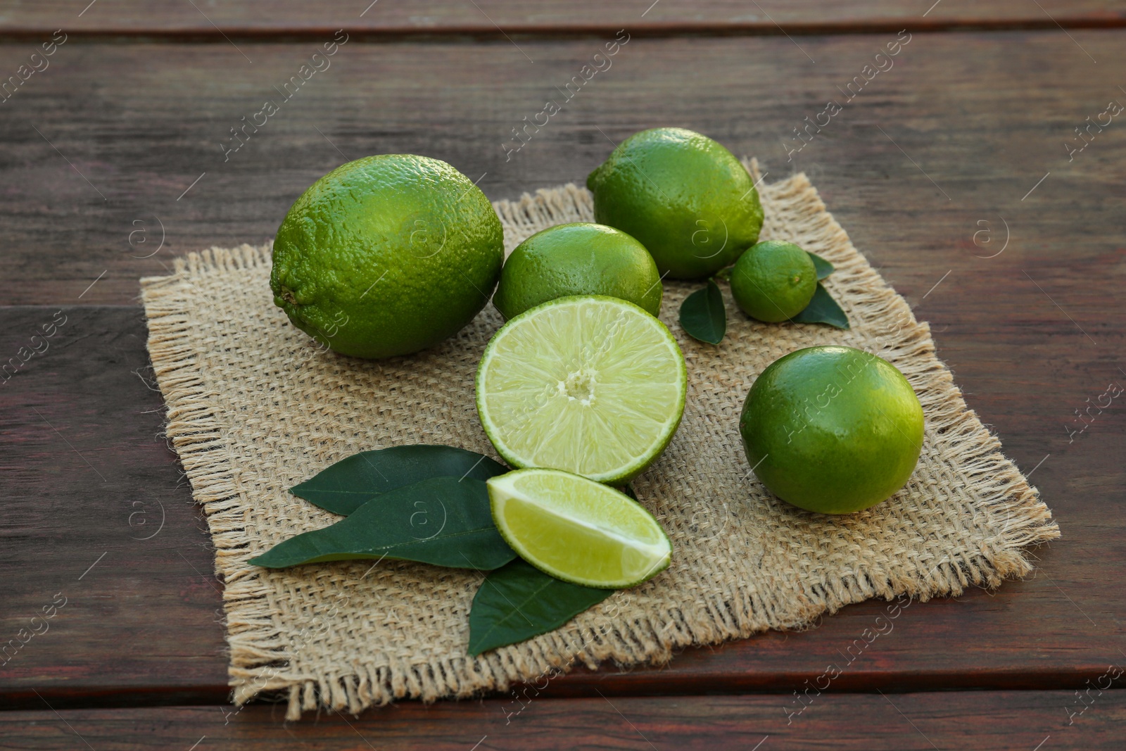 Photo of Fresh ripe limes and green leaves on wooden table