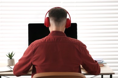 Photo of Man in headphones studying on computer indoors, back view. Online translation course