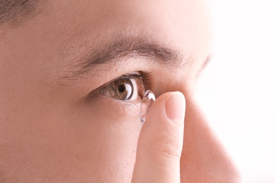 Young man putting contact lens in his eye, closeup