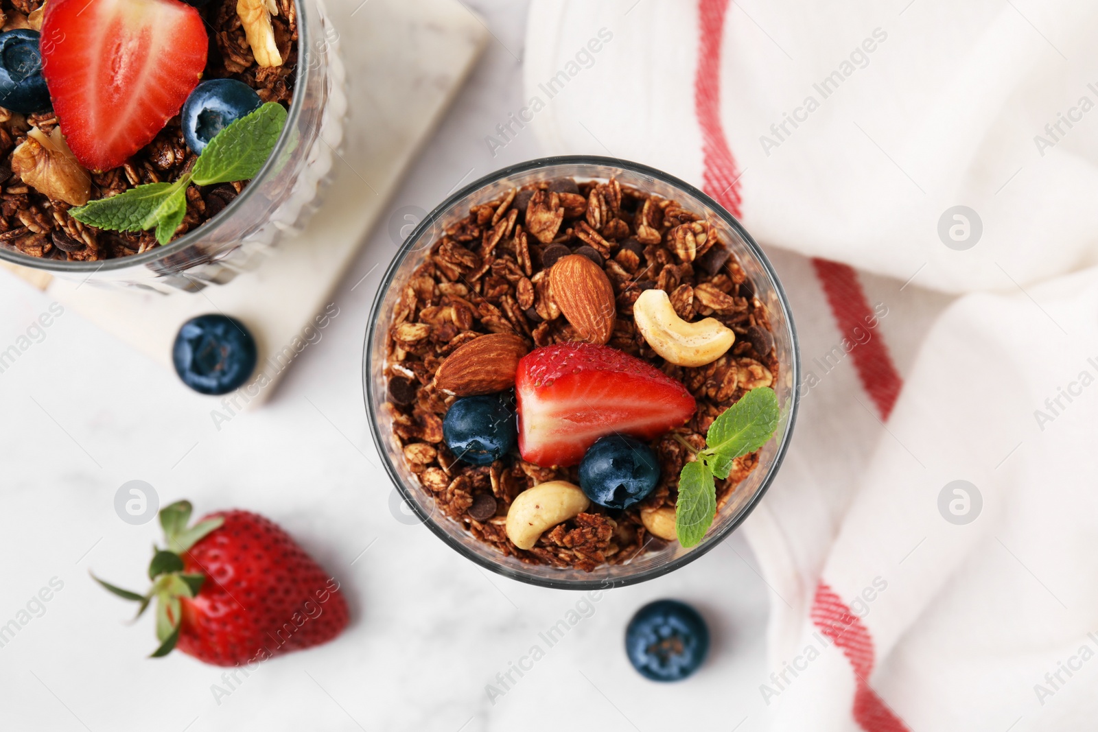 Photo of Tasty granola with berries, nuts and mint in glasses on white table, top view