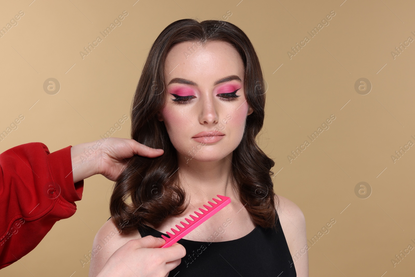 Photo of Hairdresser brushing hair of beautiful woman with comb on beige background