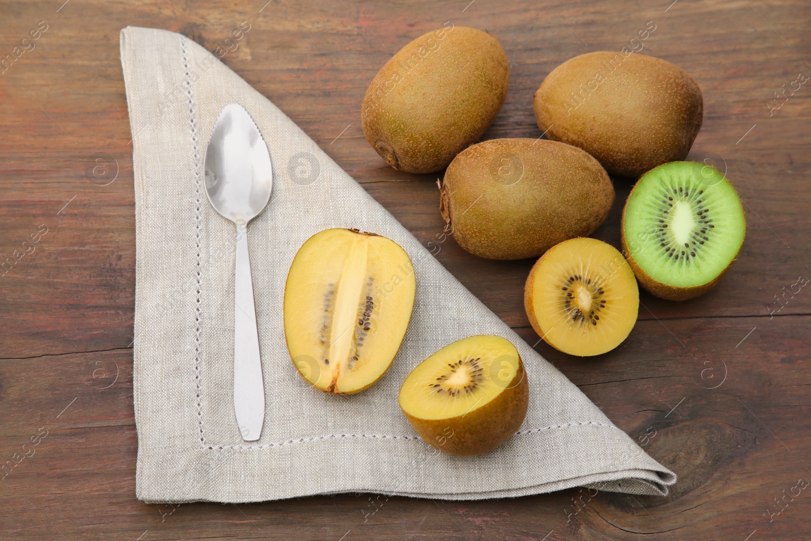 Photo of Many fresh kiwis and spoon on wooden table, above view