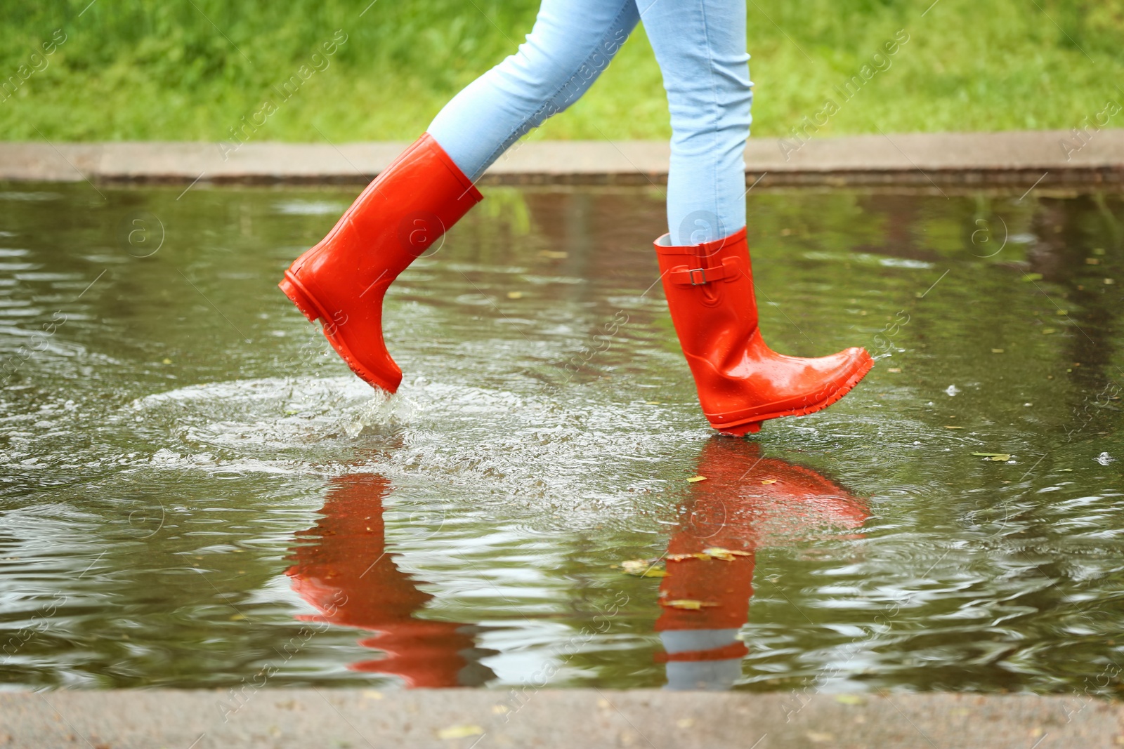 Photo of Woman with red rubber boots running in puddle, closeup. Rainy weather