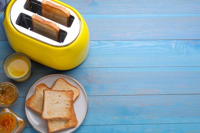 Photo of Yellow toaster with roasted bread, glass of juice and jam on light blue wooden table, flat lay. Space for text