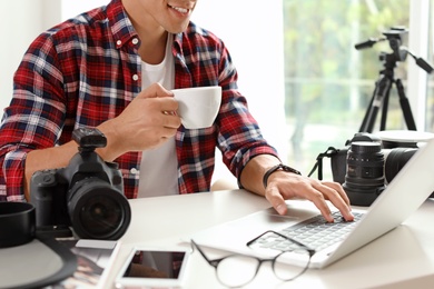 Photo of Photo blogger with laptop and cup of coffee at table indoors, closeup. Online broadcast