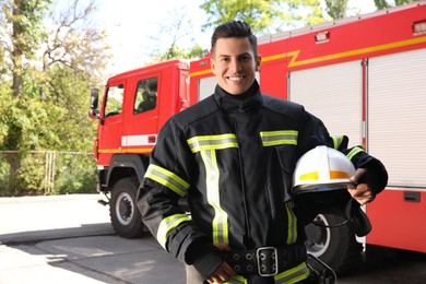 Photo of Portrait of firefighter in uniform with helmet near fire truck outdoors