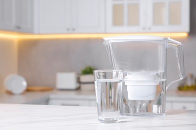 Photo of Water filter jug and glass on white marble table in kitchen, closeup. Space for text