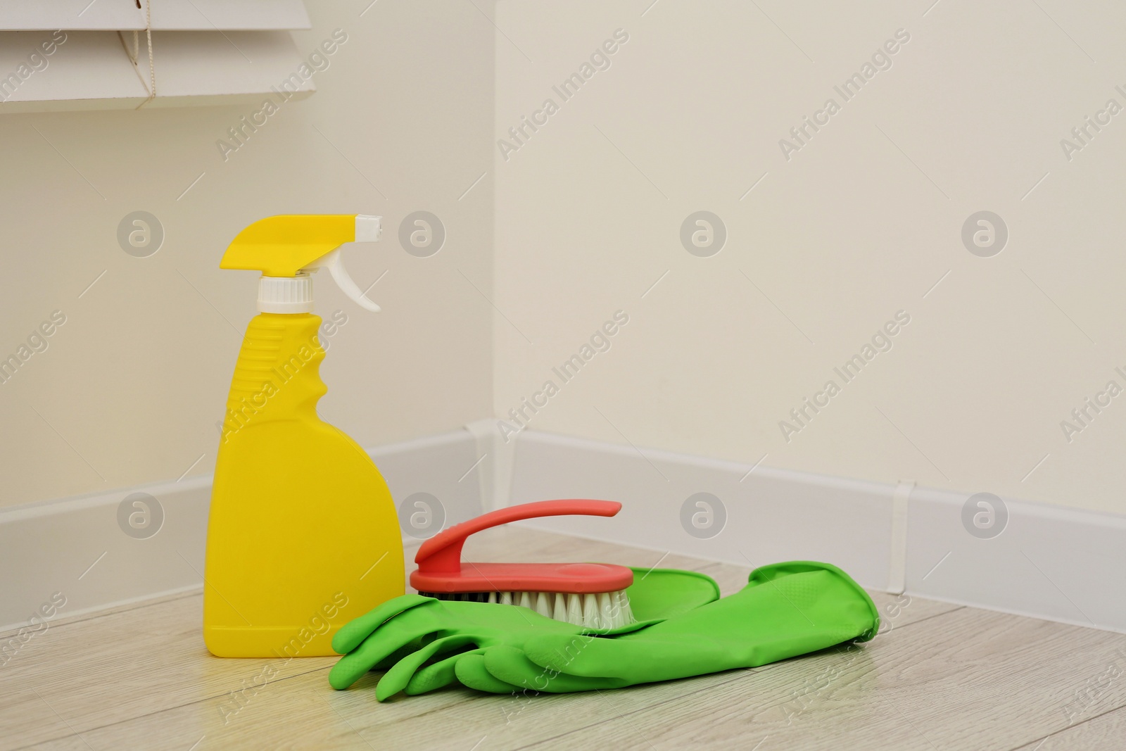 Photo of Spray bottle of cleaning product, rubber gloves and brush indoors