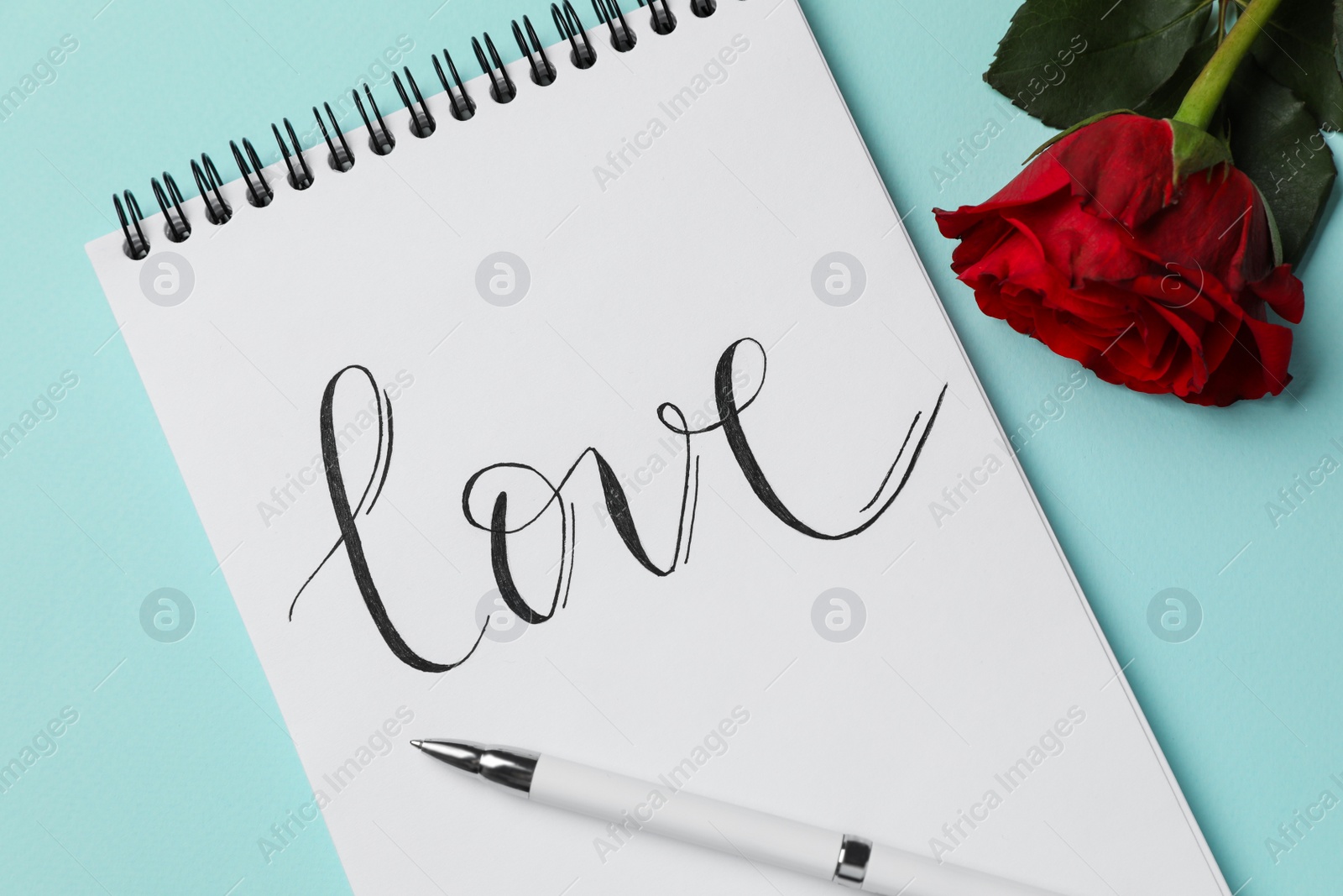 Photo of Notepad with handwritten word LOVE and rose on turquoise background, flat lay