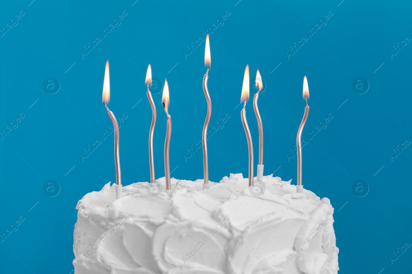 Photo of Delicious cake with cream and burning candles on light blue background, closeup