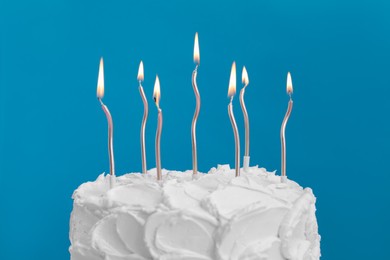 Photo of Delicious cake with cream and burning candles on light blue background, closeup