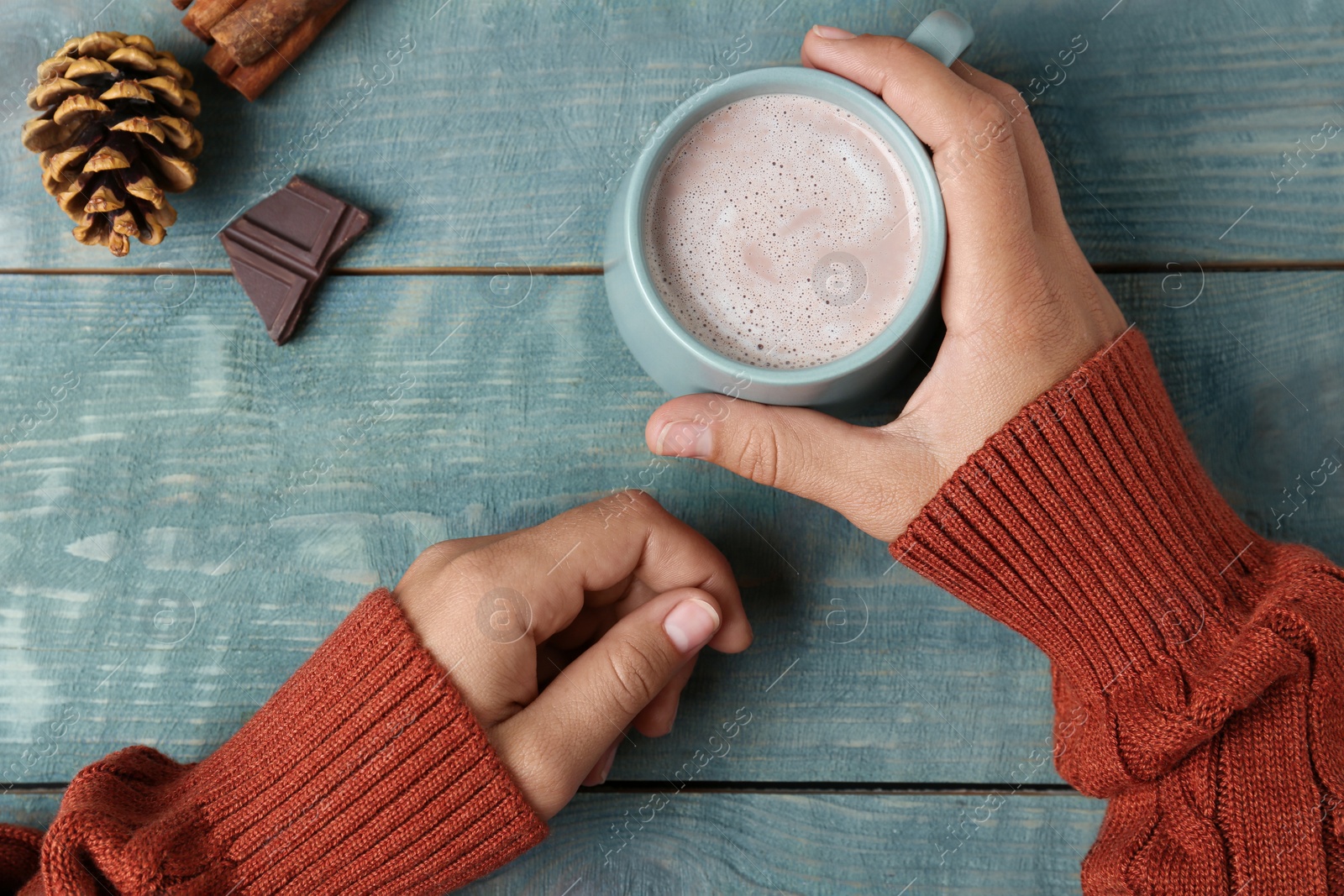 Photo of Woman holding cup of delicious cocoa drink at light blue wooden table, top view