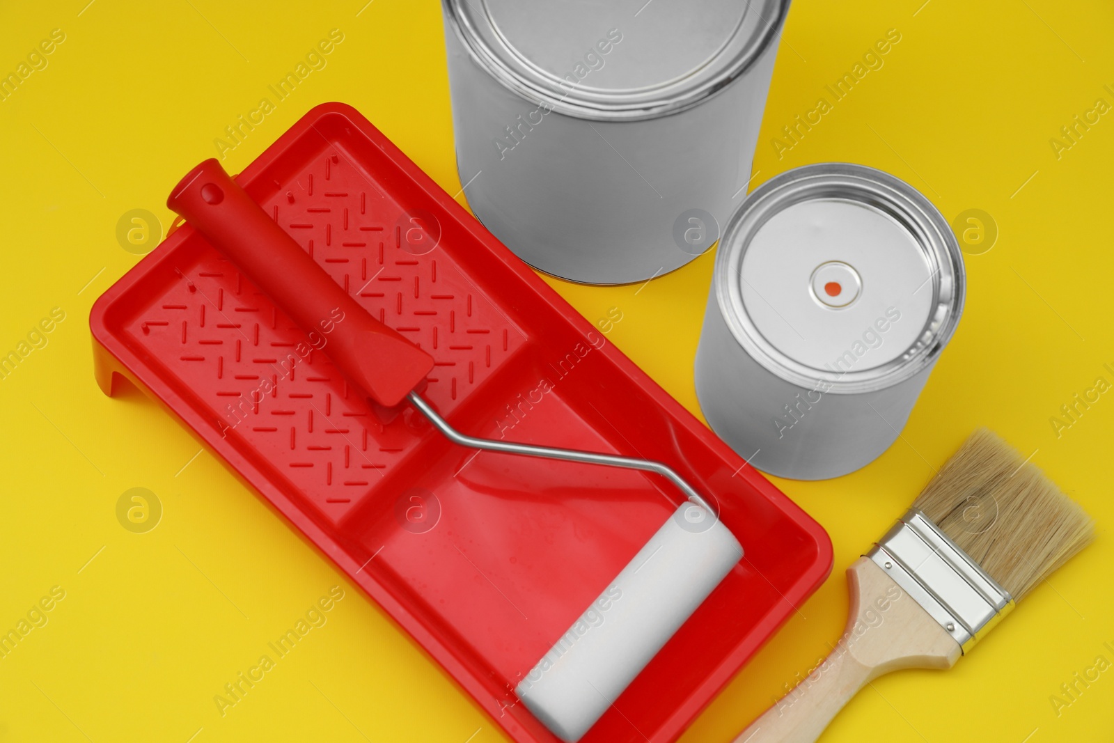 Photo of Cans of orange paint, brush, roller and container on yellow background, above view