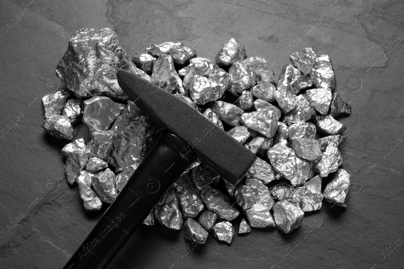 Photo of Pile of silver nuggets and hammer on black table, top view